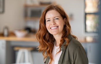 Woman with red hair smiling in a kitchen setting, wearing a green shirt.